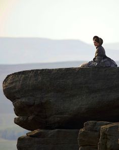 a woman sitting on top of a large rock