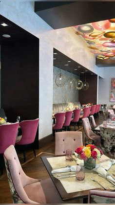 a dining room with pink chairs and white table cloths on the tables, along with colorful flowers in vases