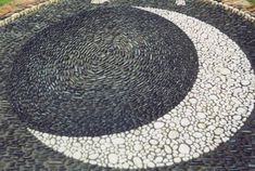 a black and white circular design made out of rocks on the ground with grass in the background