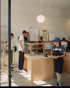 some people are standing around in a room with wood and white walls, while one person is looking at something on the counter