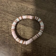 a pink and white beaded bracelet sitting on top of a wooden table next to a cell phone