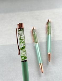 two pens sitting next to each other on top of a white surface with green leaves