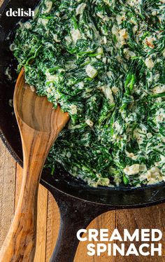 a skillet filled with spinach and cheese on top of a wooden table next to a spatula