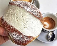 a person holding up a pastry with powdered sugar on it and two cups of coffee in the background