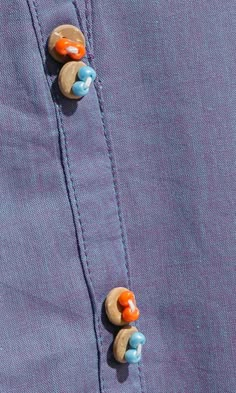 two buttons are attached to the collar of a purple shirt with blue and orange details