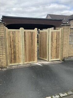 an open wooden gate on the side of a road next to a brick wall and building