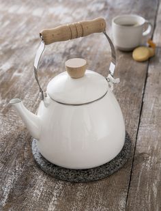 a white tea kettle with a cork handle on a wooden table next to two cups