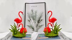 two pink flamingos are standing on top of a book with plants and grass in front of them