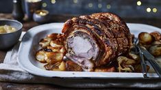 a roast beef and potatoes on a white platter with silverware next to it