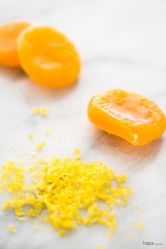 two peeled oranges sitting on top of a table next to some shredded yellow stuff