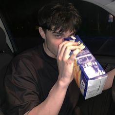 a young man sitting in the back seat of a car drinking from a carton