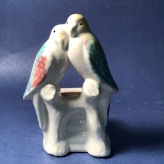 two ceramic birds sitting on top of a white elephant shaped bowl with a blue background