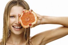 a woman holding an orange up to her face with one hand and smiling at the camera