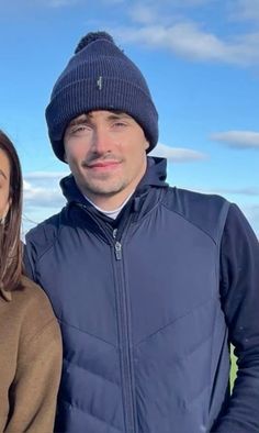 a man and woman standing next to each other in front of a blue sky with clouds