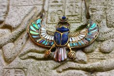 an egyptian scarp with wings and jewels on it's back, sitting on a stone wall