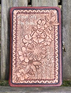 a leather case with flowers on it sitting on a wooden bench next to a fence