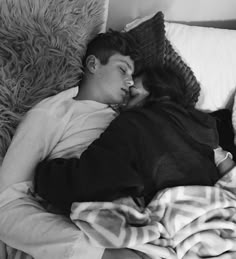 a man and woman laying in bed with blankets on top of each other, kissing