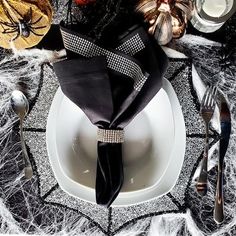 the table is set with silverware and black napkins, spider web on it