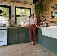 a woman standing in a kitchen next to a stove top oven and counter with pots on it