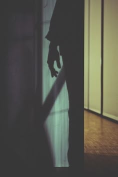 the shadow of a person standing in front of a door with their hand on the wall