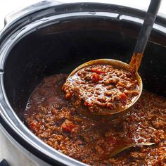 a ladle full of chili is being stirred in the slow cooker