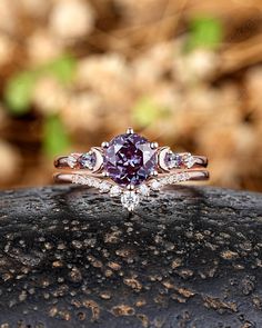 an engagement ring with three stone accents on top of a rock in front of some rocks