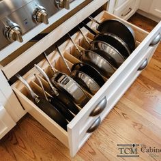 an open drawer with pots and pans in it on a wooden floor next to white cabinets