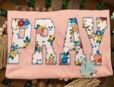 a pink bag with the word pray embroidered on it, sitting on top of a wooden chair