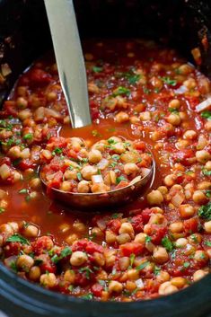 a ladle full of beans and tomatoes in a slow cooker with a spoon