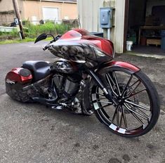 a red and black motorcycle is parked in front of a building with an open garage door