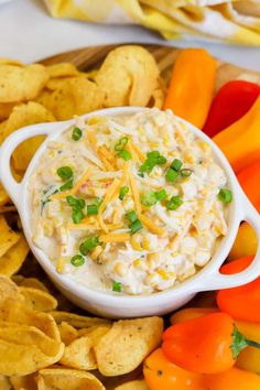 a bowl of dip surrounded by chips and veggies on a platter with cheese