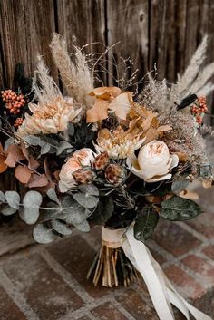 a bridal bouquet with dried flowers and foliage on a wooden table next to a fence