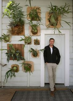 a man standing in front of a white door with plants hanging on the wall behind him