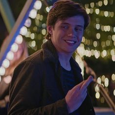 a young man smiles as he looks at his cell phone in front of a christmas tree