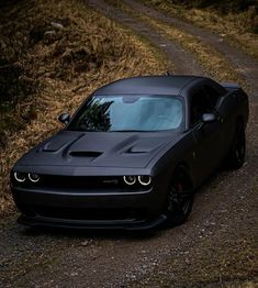 a black car parked on the side of a road next to a dirt road and grass