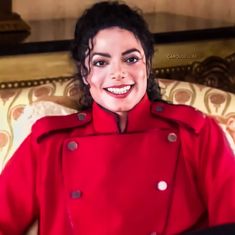 a woman in a red coat is sitting on a couch and smiling at the camera