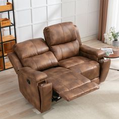 a brown reclining chair sitting on top of a wooden floor next to a table