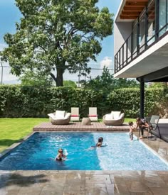 people are playing in the pool next to an outdoor deck and lounge area with chairs