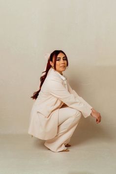 a woman kneeling down with her hands on her hips and legs crossed, wearing a white suit