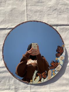 a person taking a selfie in front of a circular mirror with butterflies on it