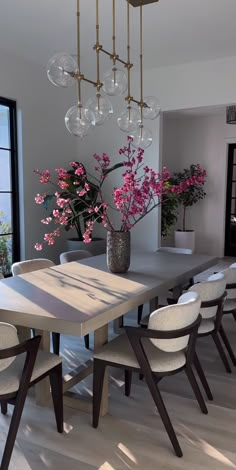 a dining room table with white chairs and a large vase filled with flowers on it