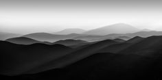 black and white photograph of mountains in the distance with fog coming from them, taken on an overcast day