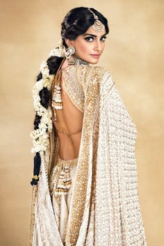 a woman in a white sari and headpiece with flowers on her hair is posing for the camera