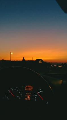 the dashboard of a car at sunset with an orange glow in the sky behind it