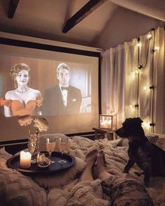 a dog sitting on a bed watching a movie in front of a screen with candles