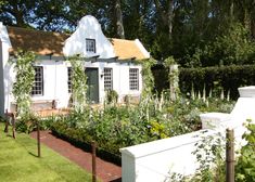 a white house sitting next to a lush green field with lots of flowers on it