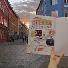 a person holding up an open book in the middle of a cobblestone street