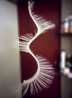 a white string art piece hanging from the side of a glass door in front of a bookshelf