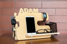 an apple watch, cell phone and glasses are on a wooden stand with the word adam attached to it