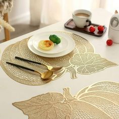 a white table topped with plates and gold utensils next to a cup of coffee